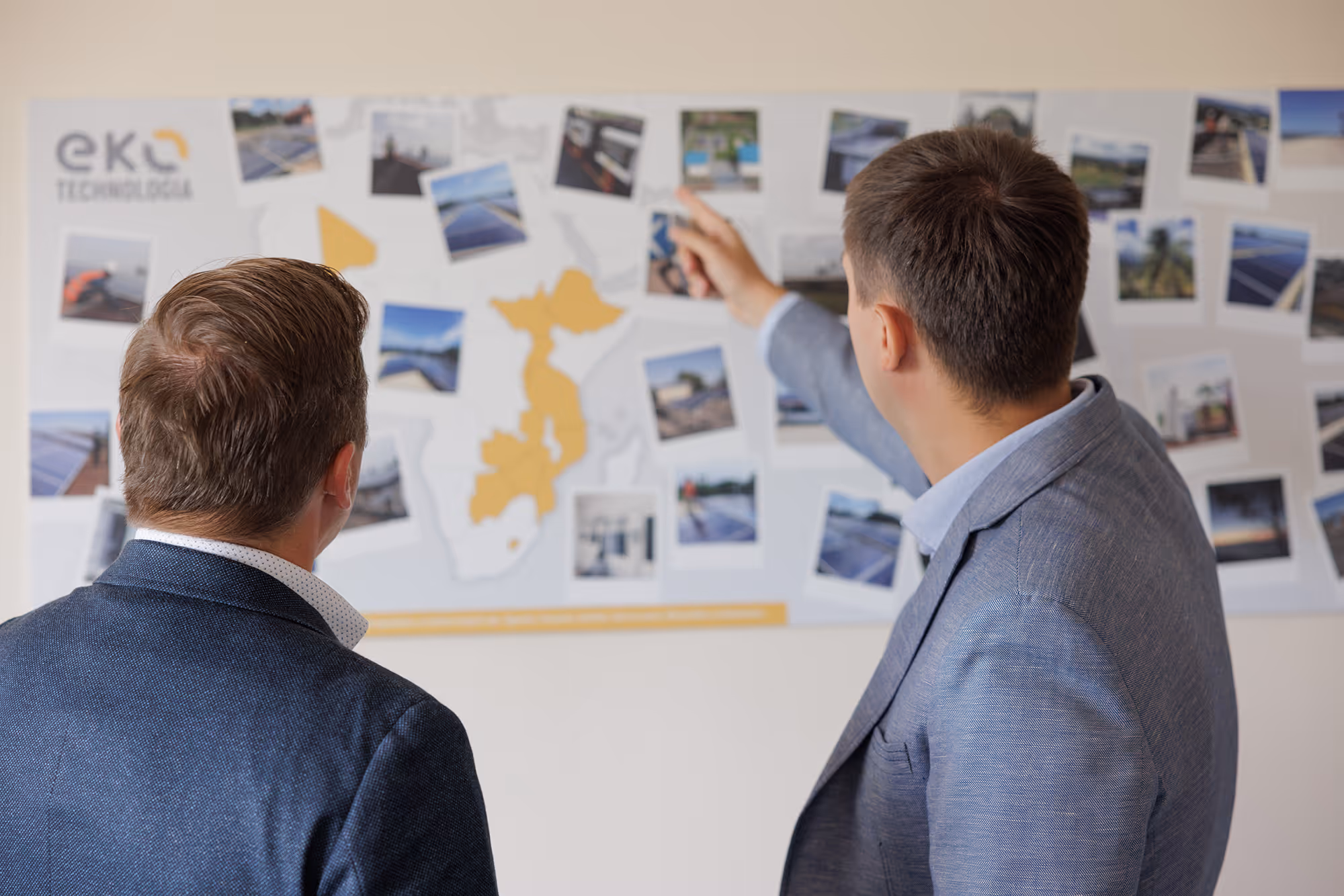 Dwaj mężczyźni w garniturach analizują mapę z zaznaczonymi miejscami realizacji projektów energetycznych i zdjęciami instalacji w Afryce.